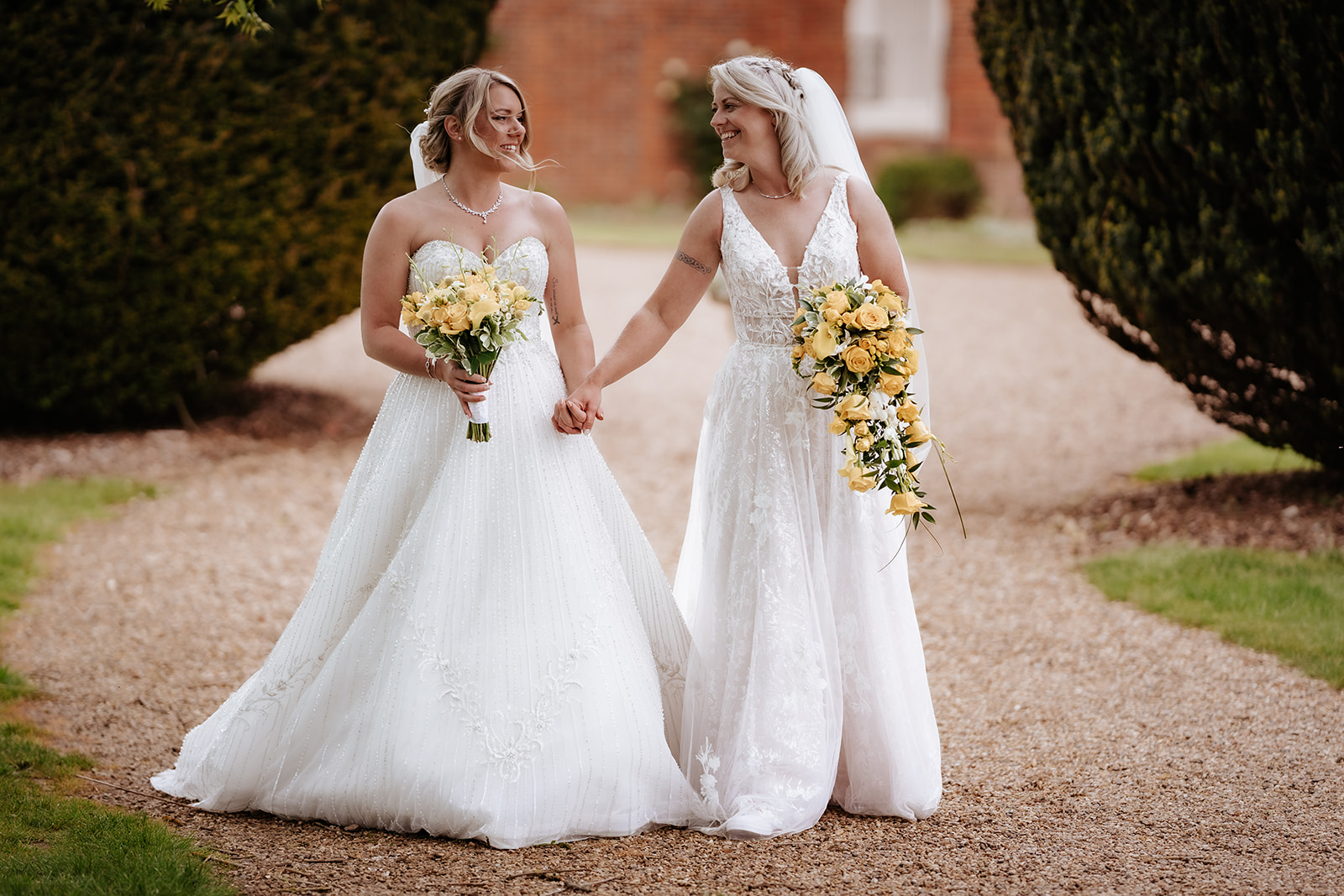 Two brides walking hand-in-hand through the autumn parkland at Gosfield Hall wedding venue in Essex — LGBTQ+ wedding photography by Lily & White