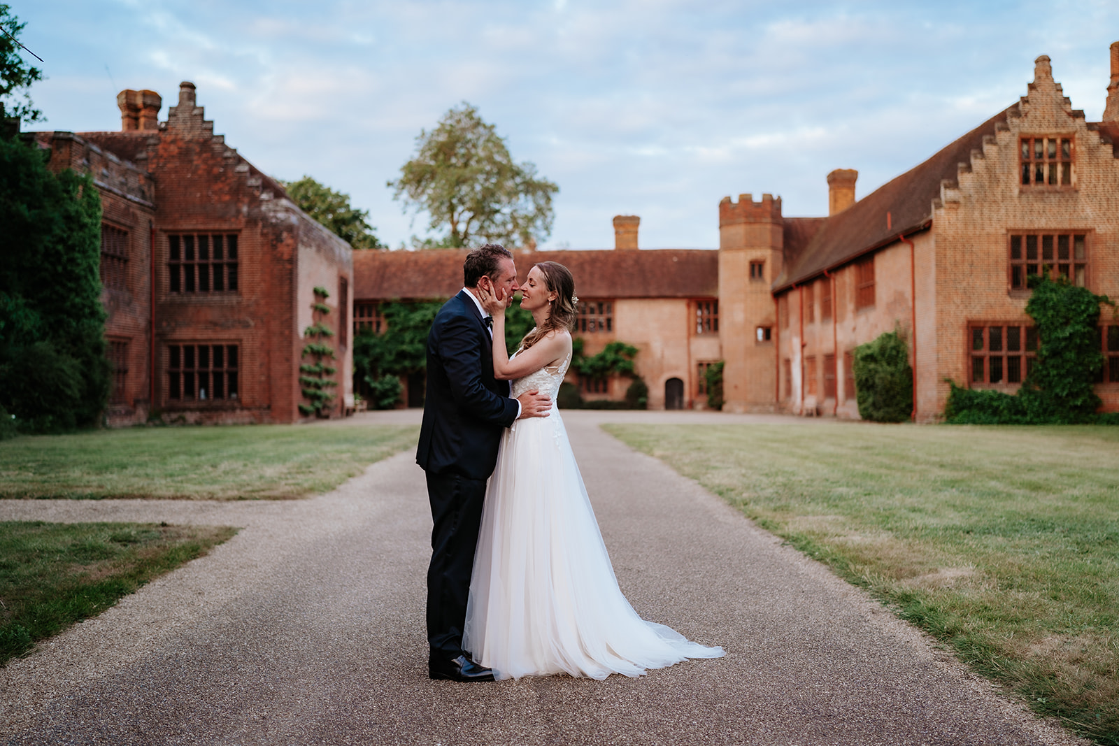 Bride and groom sharing an intimate moment in the courtyard at Ingatestone Hall, Essex, at blue hour — editorial wedding portrait by Lily & White Essex wedding photographer