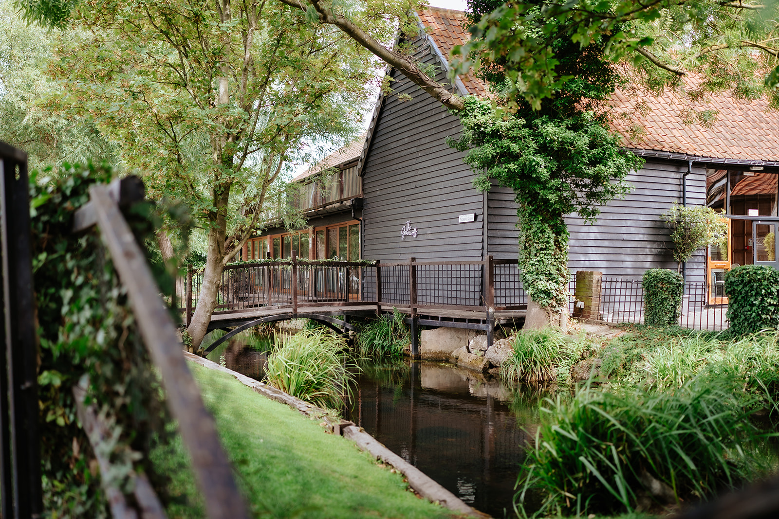 The converted barn and wooden bridge over the stream at Old Brook Barn wedding venue in Essex — photographed by Lily & White