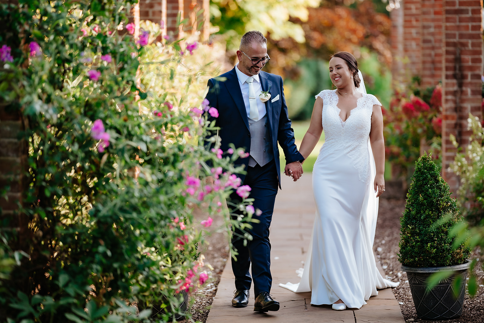 Bride and groom walking through flowering gardens at Hutton Hall in Brentwood, Essex — natural wedding photography by Lily & White