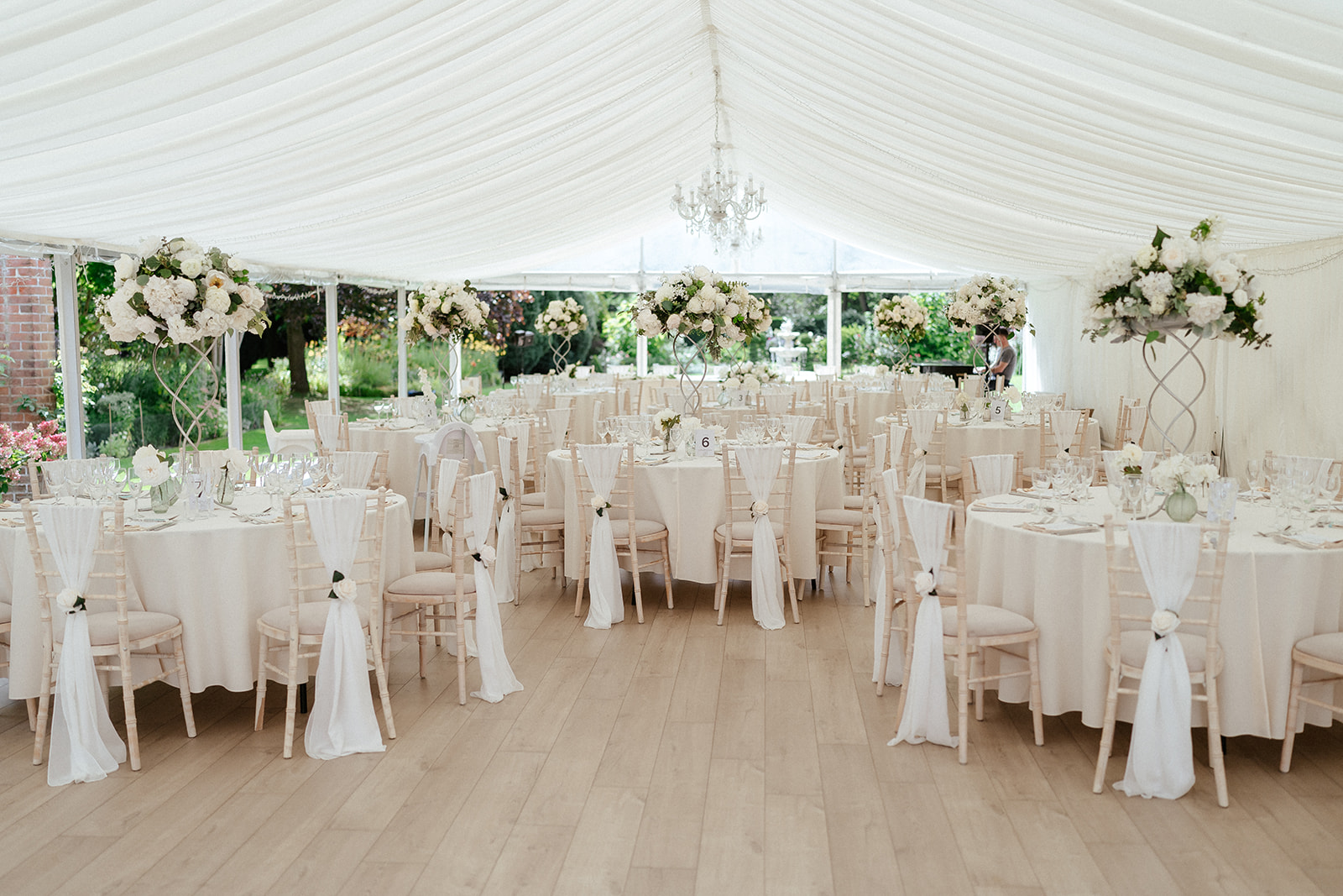 Elegant white marquee reception setup at Hutton Hall wedding venue in Brentwood with draped ceiling, crystal chandelier, and tall floral centerpieces — wedding photography by Lily & White