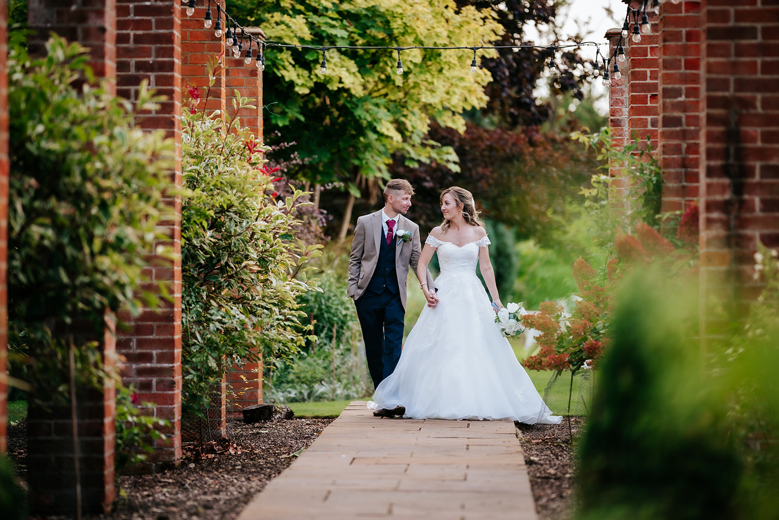 Bride and groom walking through gardens at Hutton Hall wedding venue in Brentwood — natural documentary photography by Lily & White