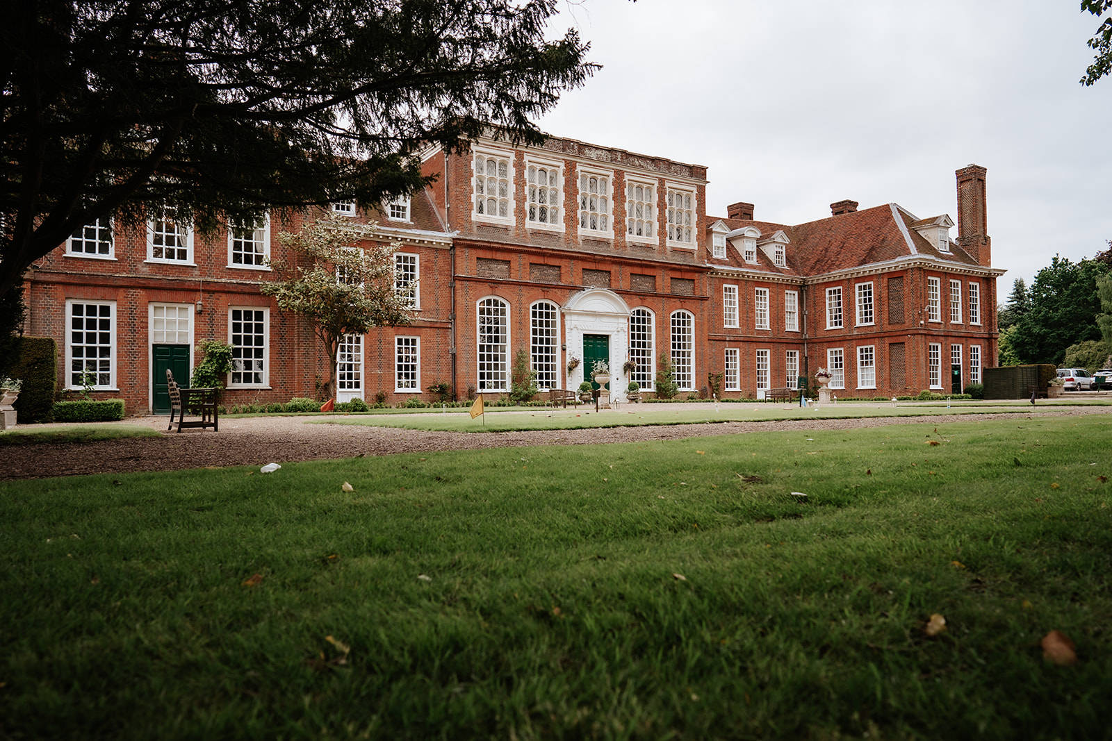 The Georgian redbrick facade of Gosfield Hall wedding venue with formal lawns and mature trees in Essex countryside — photographed by Lily & White