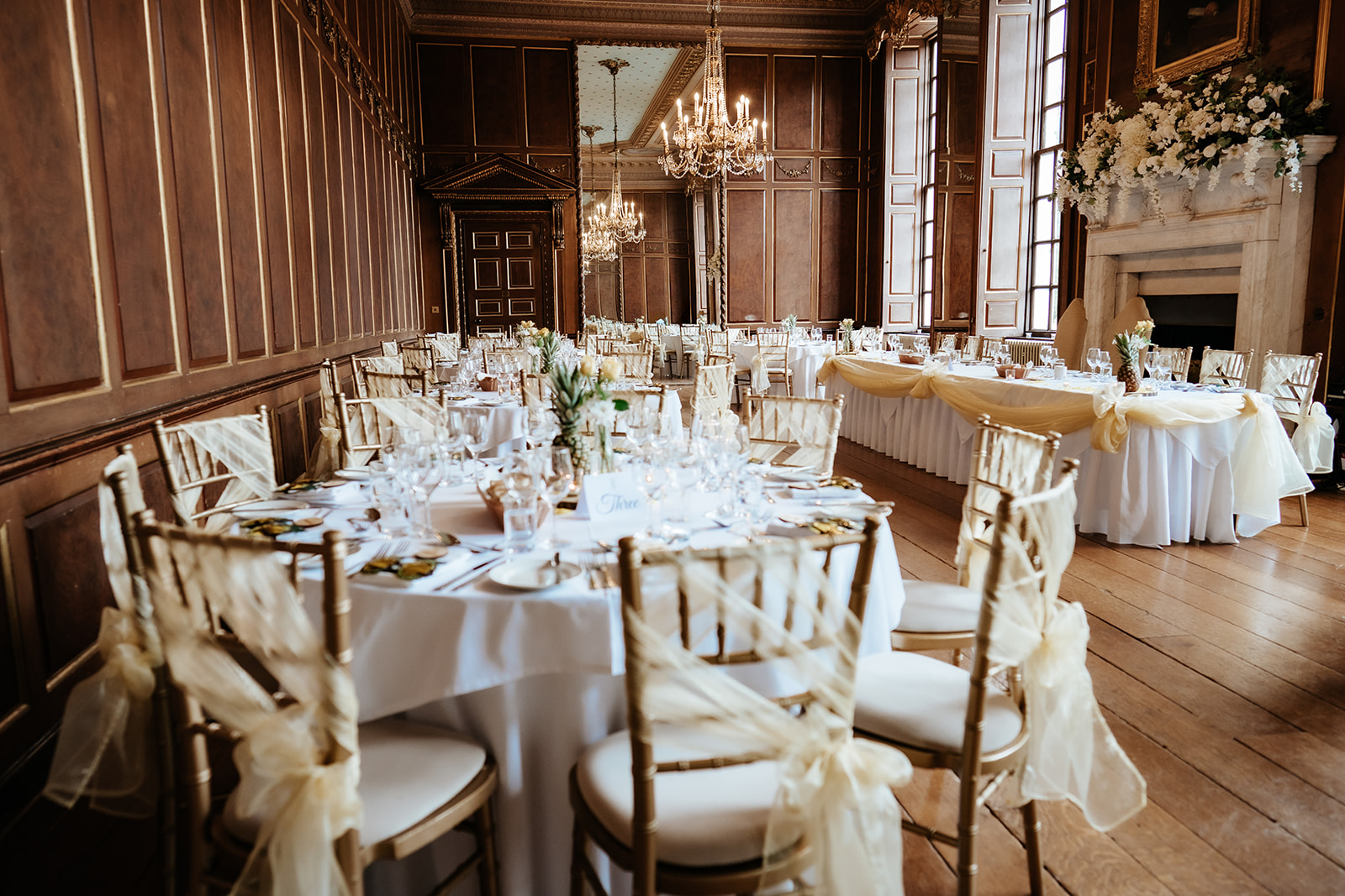 The ballroom at Gosfield Hall set for wedding breakfast with crystal chandeliers, oak panelling, and elegant table settings — photographed by Lily & White