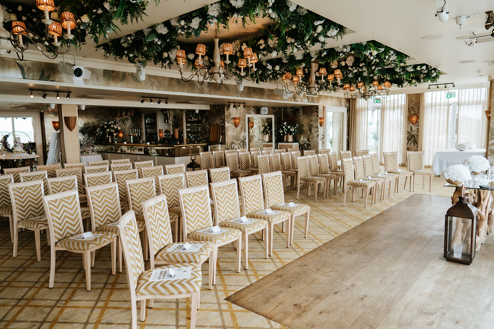 The Tides Ballroom at The Roslin Beach Hotel, Southend-on-Sea, set for a wedding ceremony with elegant chevron chairs and a stunning floral ceiling installation