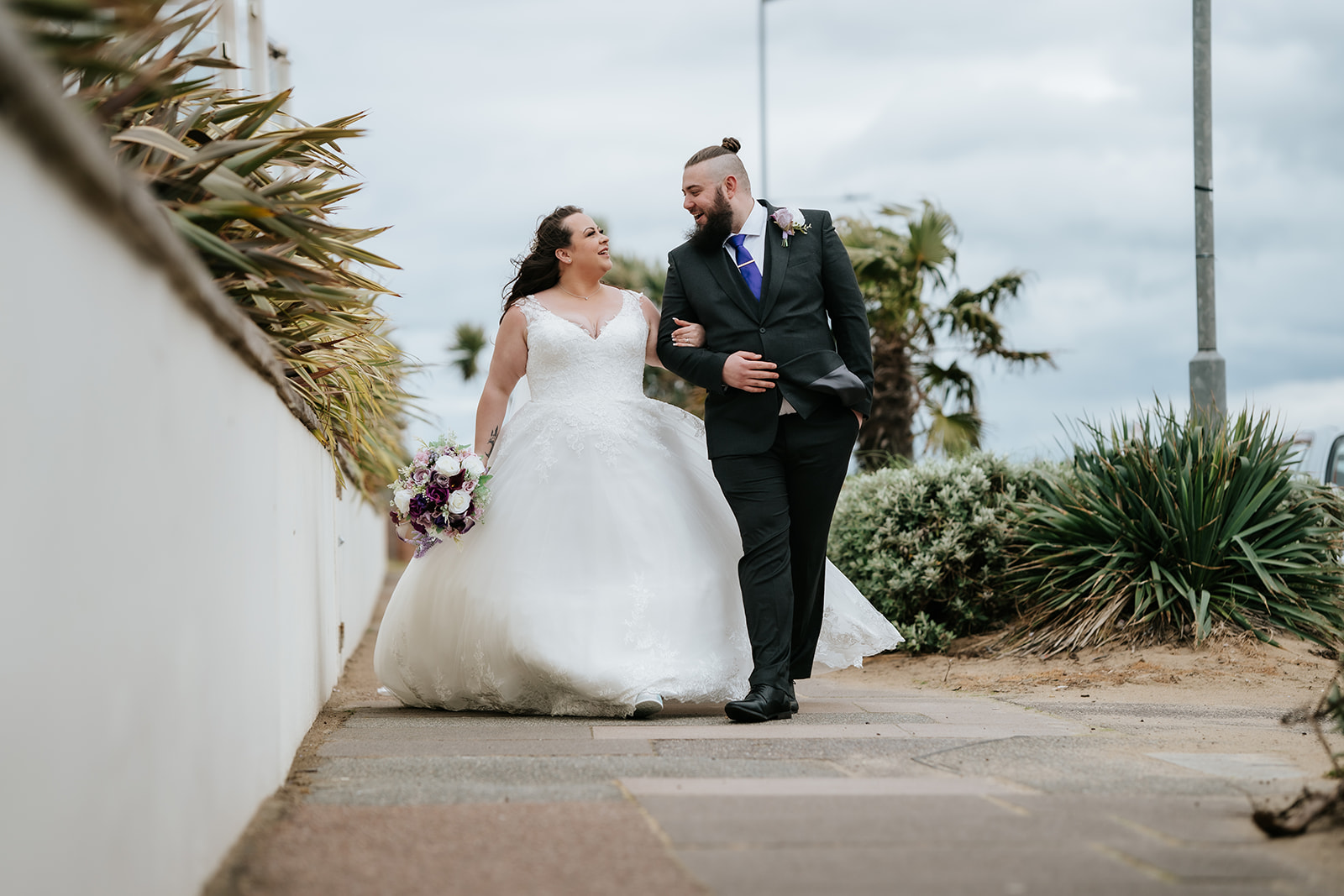Bride and groom walking together along the coastal terrace at The Roslin Beach Hotel in Thorpe Bay, Southend-on-Sea, with the Thames Estuary visible behind them — editorial wedding photography by Lily & White