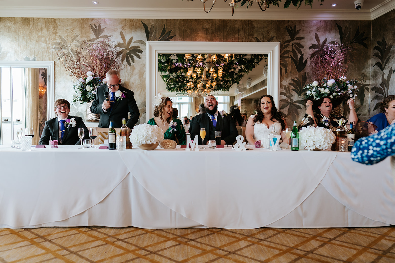 Candid documentary photograph of the wedding breakfast at The Roslin Beach Hotel, Southend-on-Sea, capturing the top table during speeches in the elegantly decorated dining room — Lily & White wedding photography