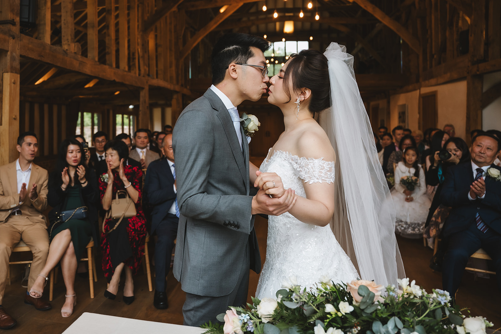 Yiran and Jeffrey sharing their first kiss during their wedding ceremony in the Hay Barn – wedding photography by Tel, Lily & White