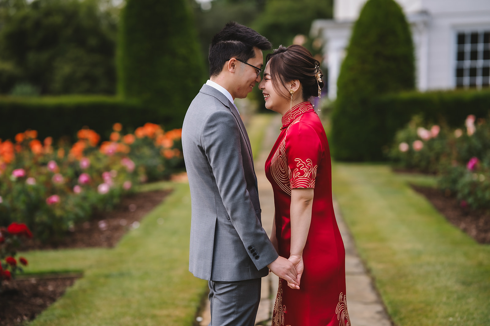 Yiran and Jeffrey holding hands in the rose garden at Blake Hall, Yiran in her red qipao.