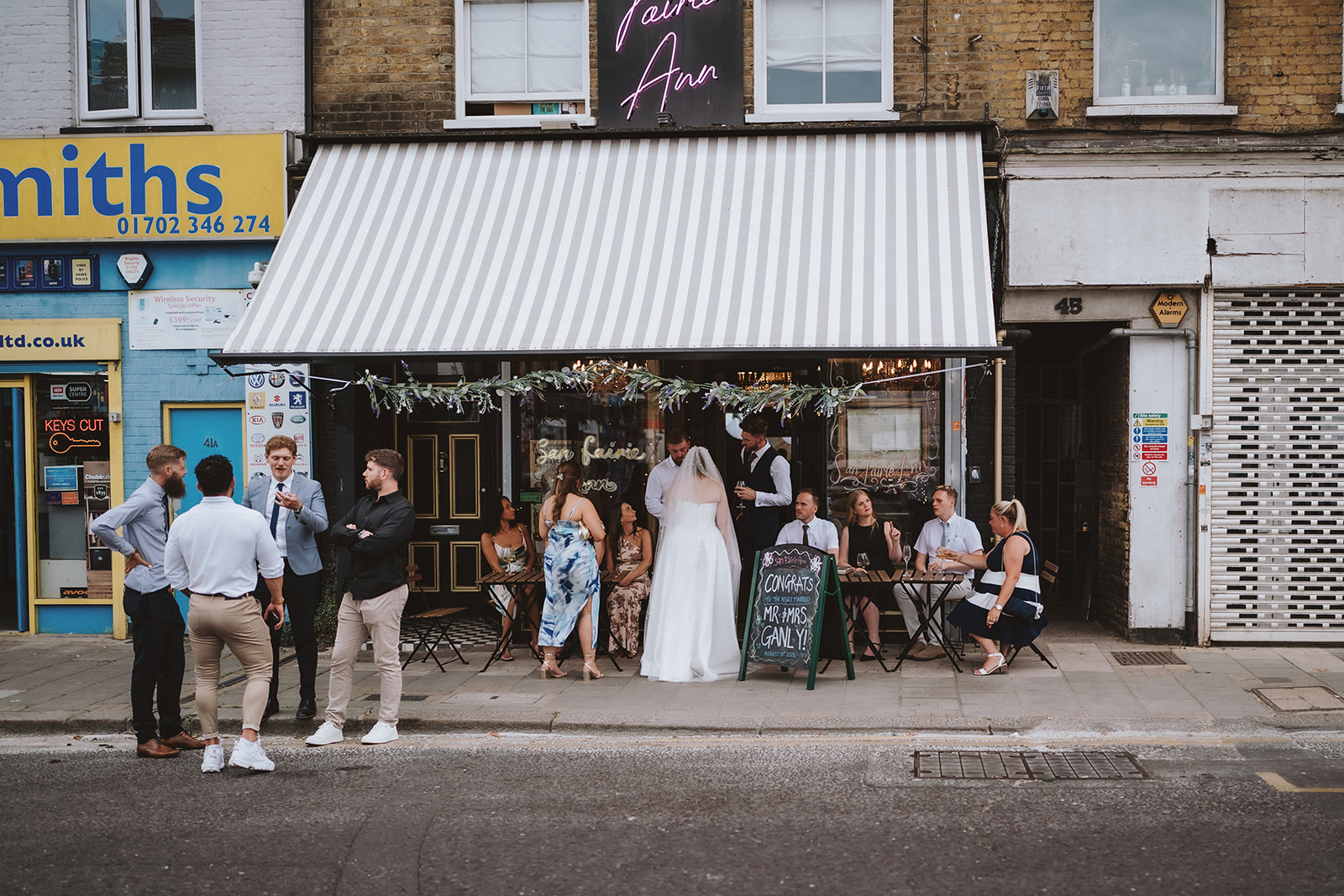 Candid documentary wedding photograph outside San Fairie Ann bar in Southend, capturing the bride and groom with guests during an relaxed urban wedding celebration on the high street — editorial wedding photography by Lily & White