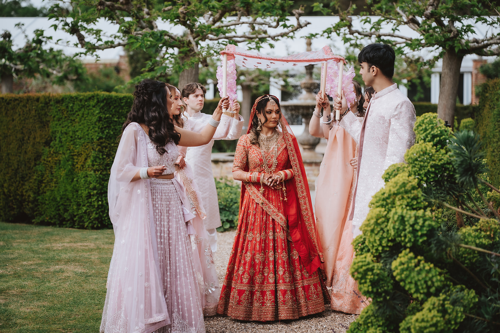 Bride Honica in traditional red and gold lehenga during the Hindu ceremony in the Walled Garden at Braxted Park Essex