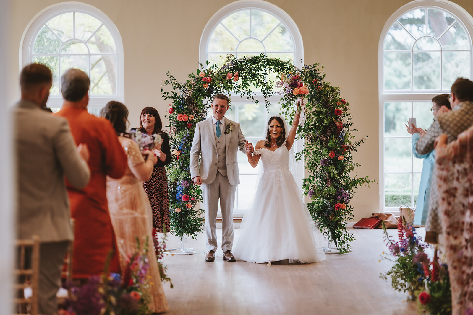 Civil ceremony in The Orangery at Braxted Park - Honica and Ben beneath a floral arch at their fusion wedding Essex