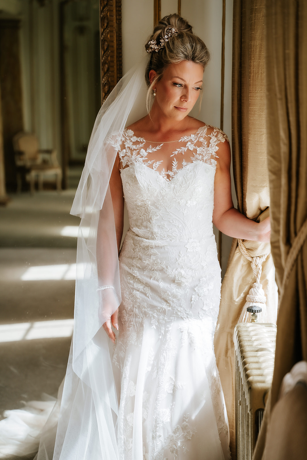 Bride in lace wedding dress looking through period doorway at Gosfield Hall — natural light bridal portrait by Lily & White