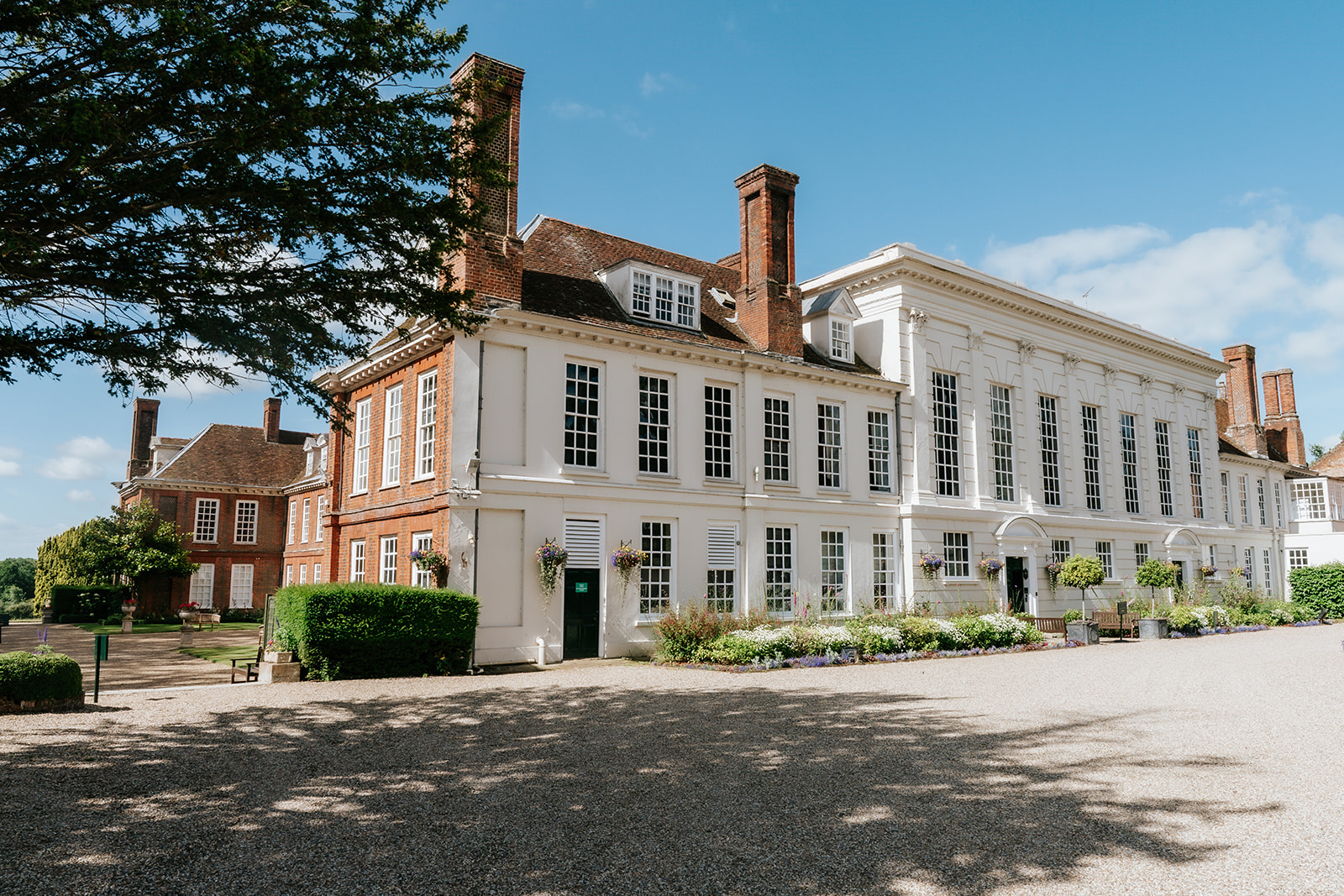 The front facade of Gosfield Hall wedding venue in Essex showing the elegant white Georgian wing and Tudor redbrick architecture — photographed by Lily & White
