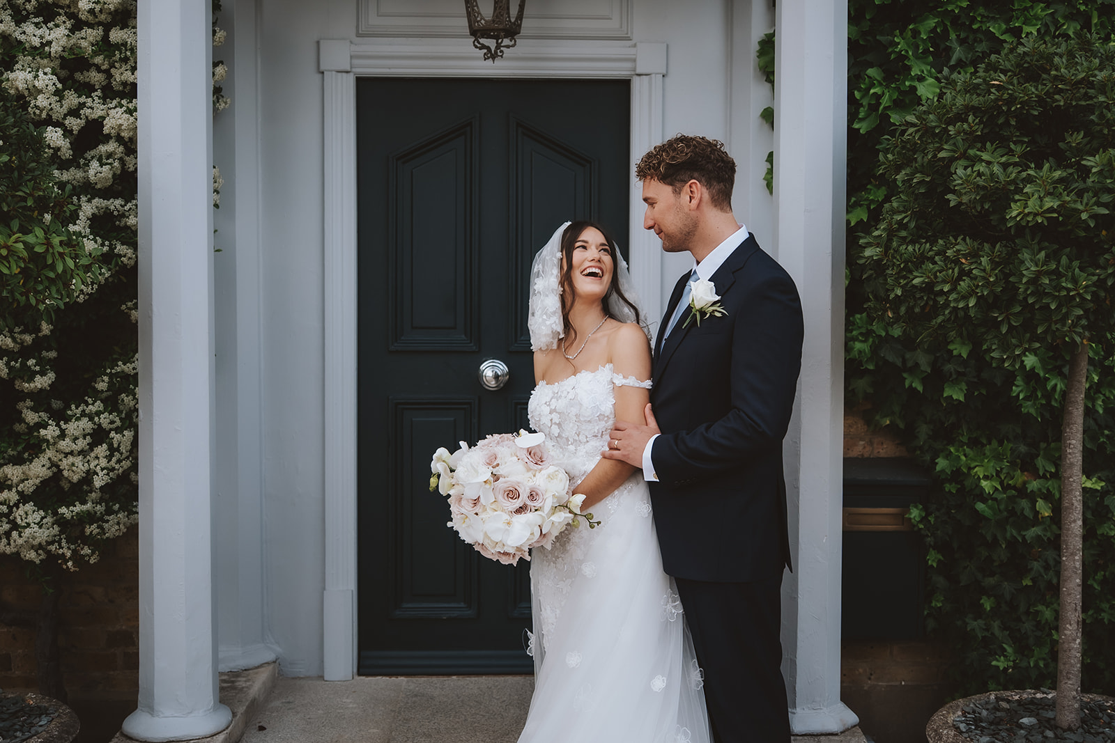 Bride laughing with groom in front of elegant columned entrance at a Brentwood wedding venue — candid moment captured by Lily & White Photography