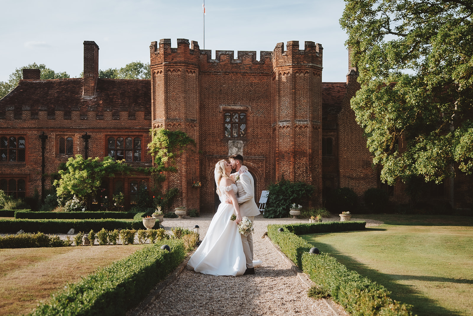 Bride and groom walking along the formal gardens at Leez Priory wedding venue with the Tudor mansion facade behind them — editorial wedding photography by Lily & White