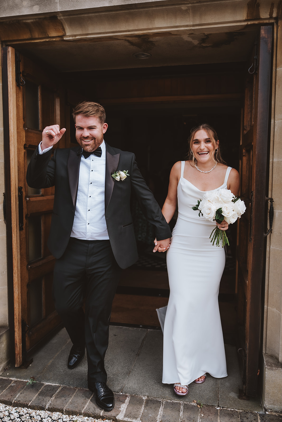 Editorial wedding photographer Essex; a joyful bride and groom holding hands while exiting a stone church after their ceremony.