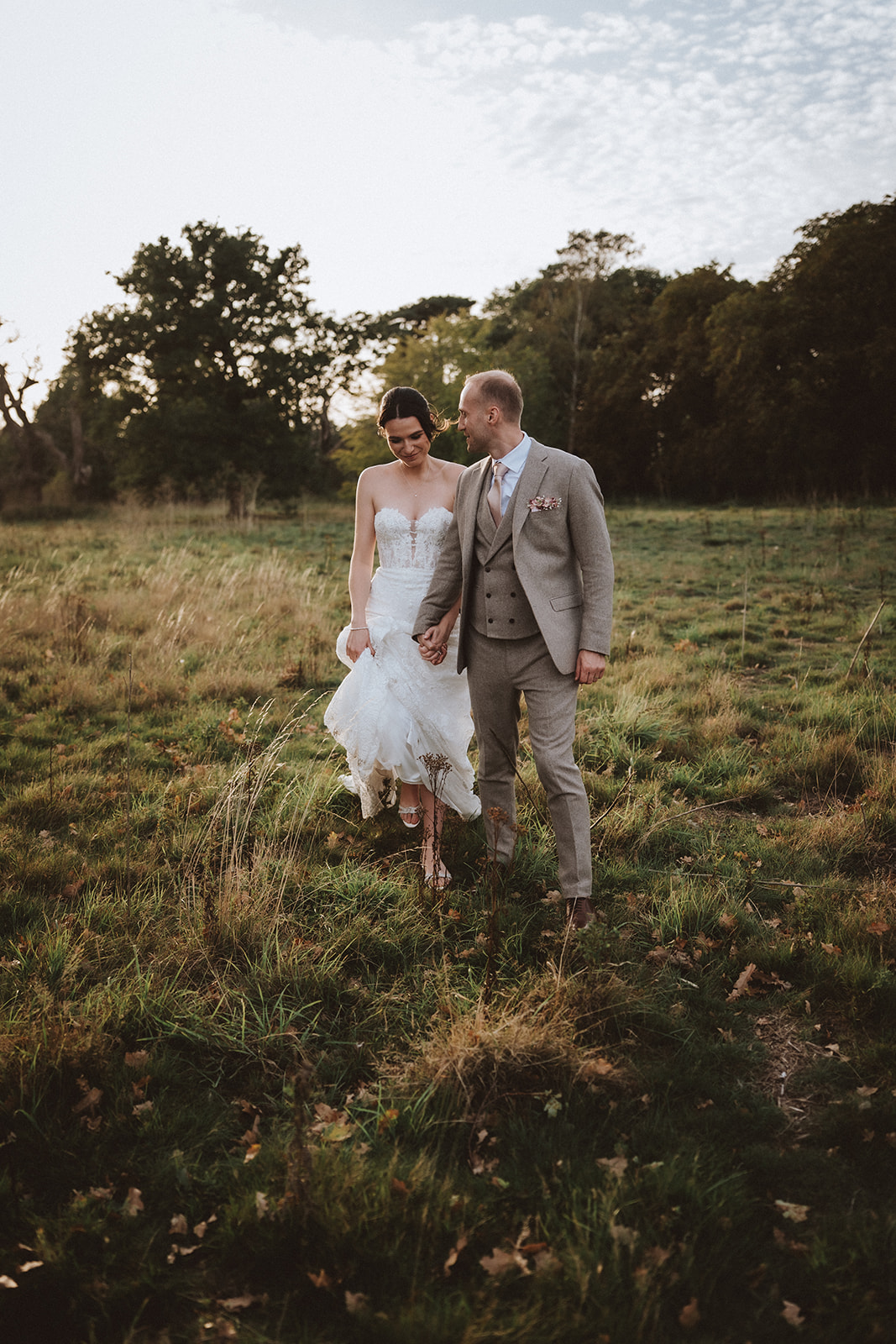 Romantic and unscripted wedding photography in a wild Essex meadow, showing a bride and groom walking together at sunset.