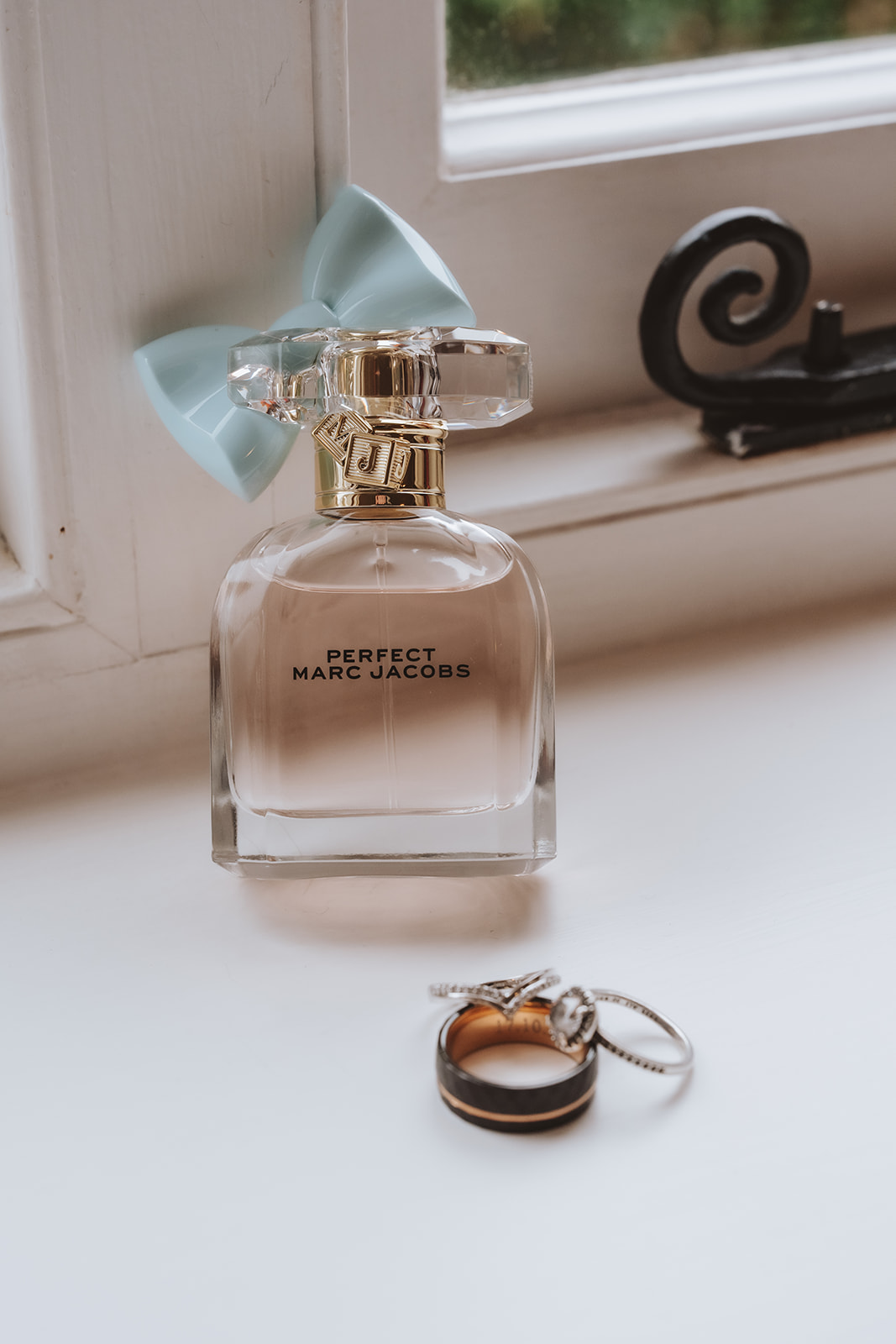Editorial wedding photography detail; Marc Jacobs perfume bottle and wedding rings on a minimalist white windowsill.