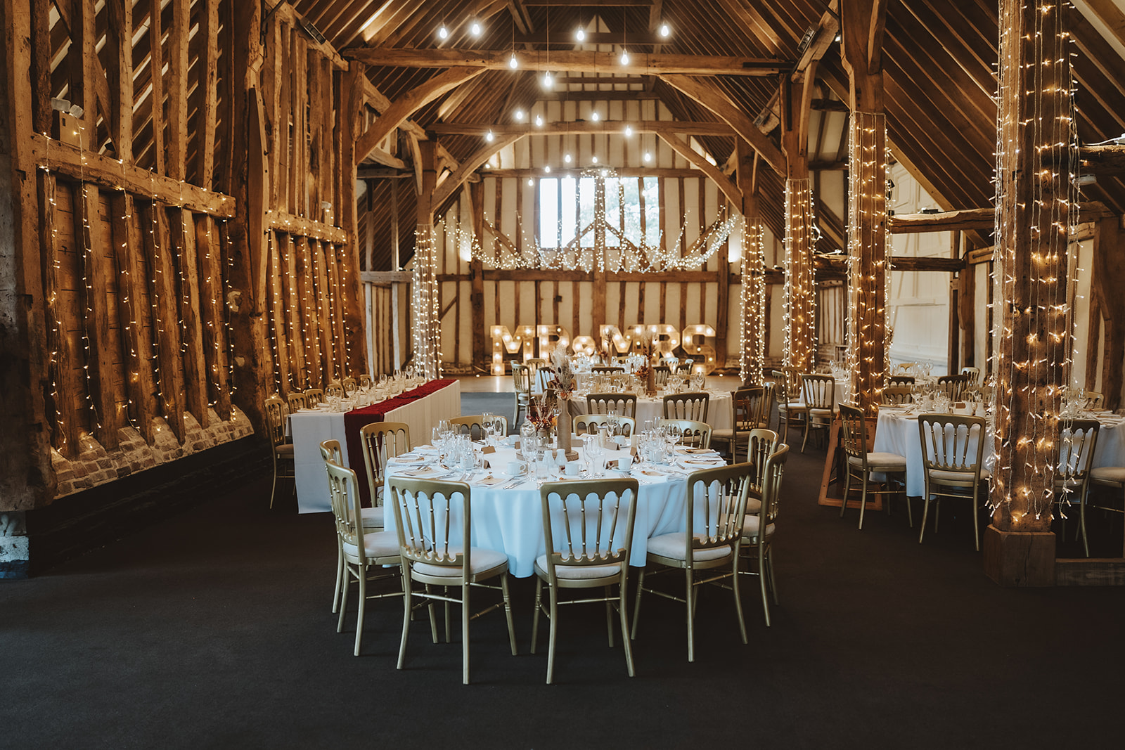the Essex Barn at Blake Hall dressed for an evening reception with fairy lights, gold Chiavari chairs and illuminated Mr & Mrs lettering.
