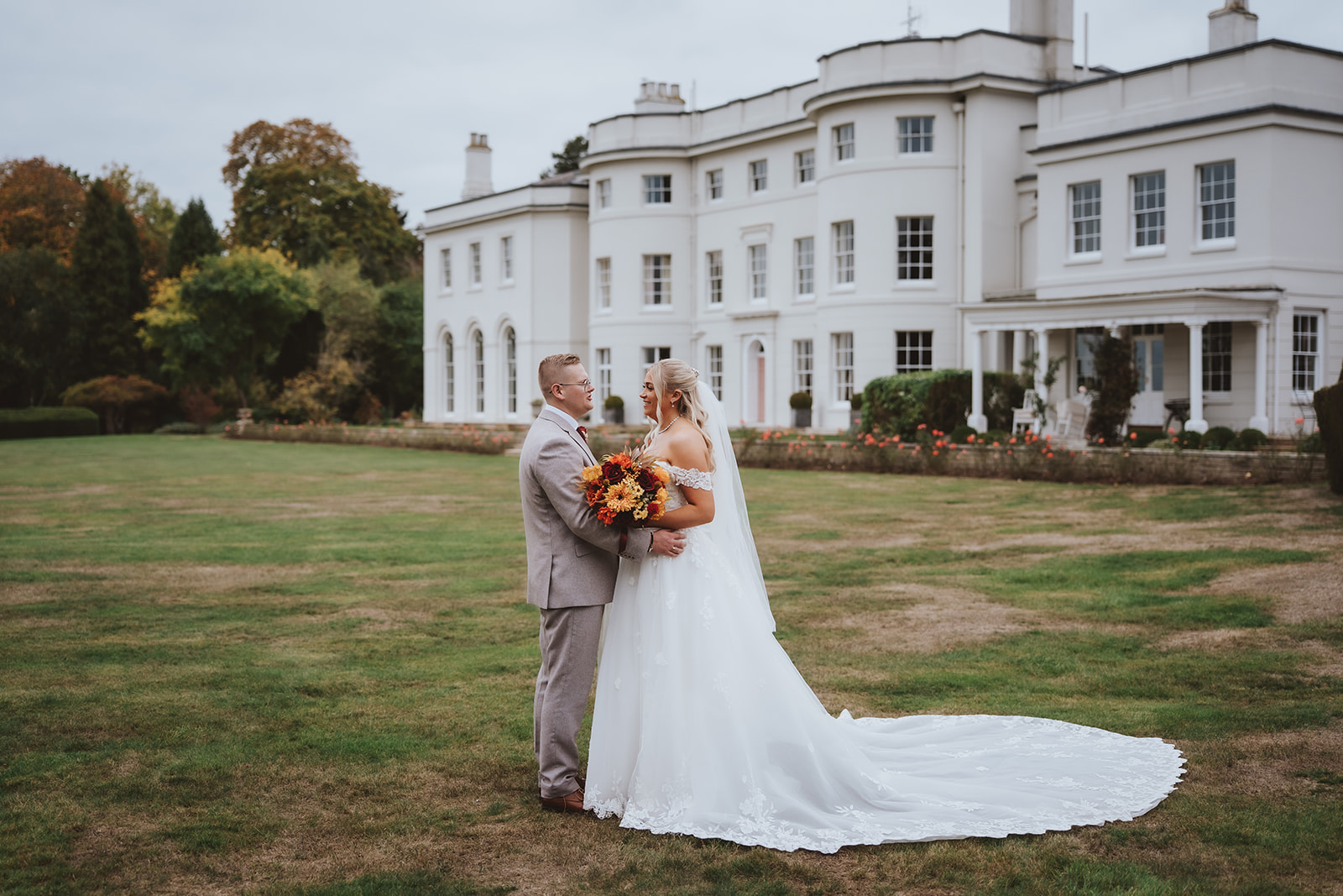 a couple embracing on the lawn in front of Blake Hall manor house in autumn.