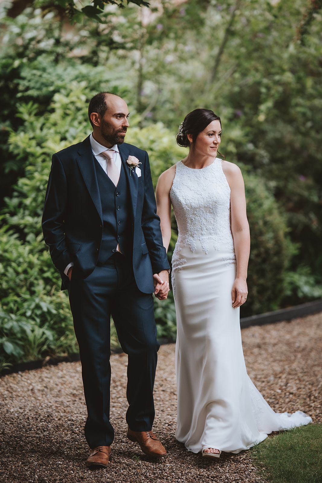 Editorial wedding photography at Leez Priory in Essex, capturing a bride and groom walking hand-in-hand past the historic Tudor tower and brickwork of the manor house.